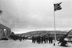 Sivile og soldater ved flaggstang i Åsegarden leir.