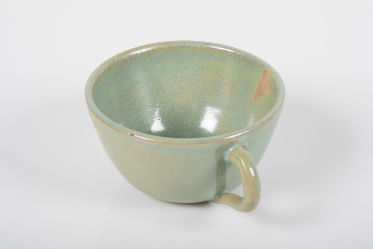 Kopp keramikk med grønn lasur. Buet hank på koppen. Bunnen har matt overflate.