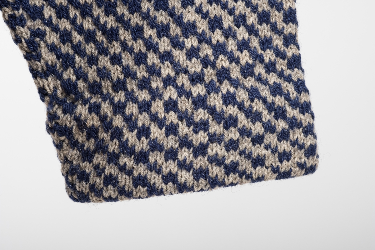 Blå og grå strikket herregenser. 
To knapper ved halsåpningen for å kunne kneppe den igjen. 
Ermekantene er brettet innover og sydd fast. 
To sømkanter på baksiden av genseren.