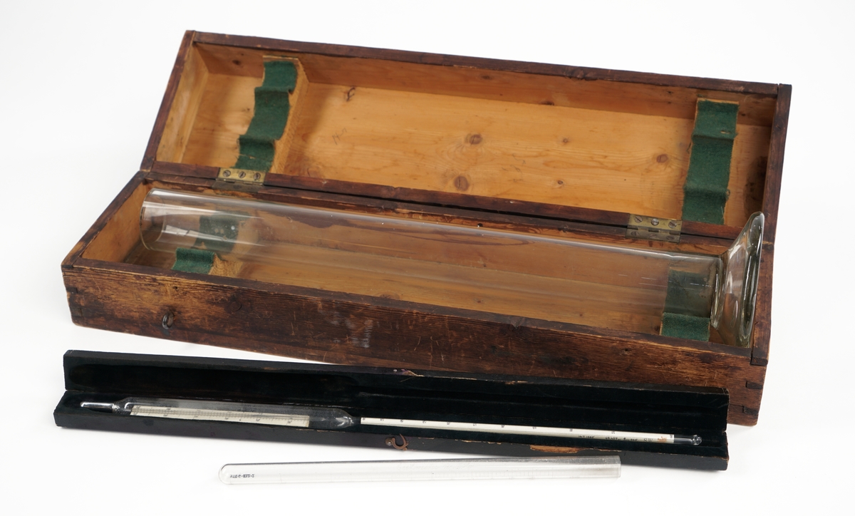 Alkoholmeter/termometer i etui samt glasskolbe og reagensrør. Måleinstrumentet hører ikke til kassen opprinnelig, men fungerer som en erstatning for opprinnelig instrument.