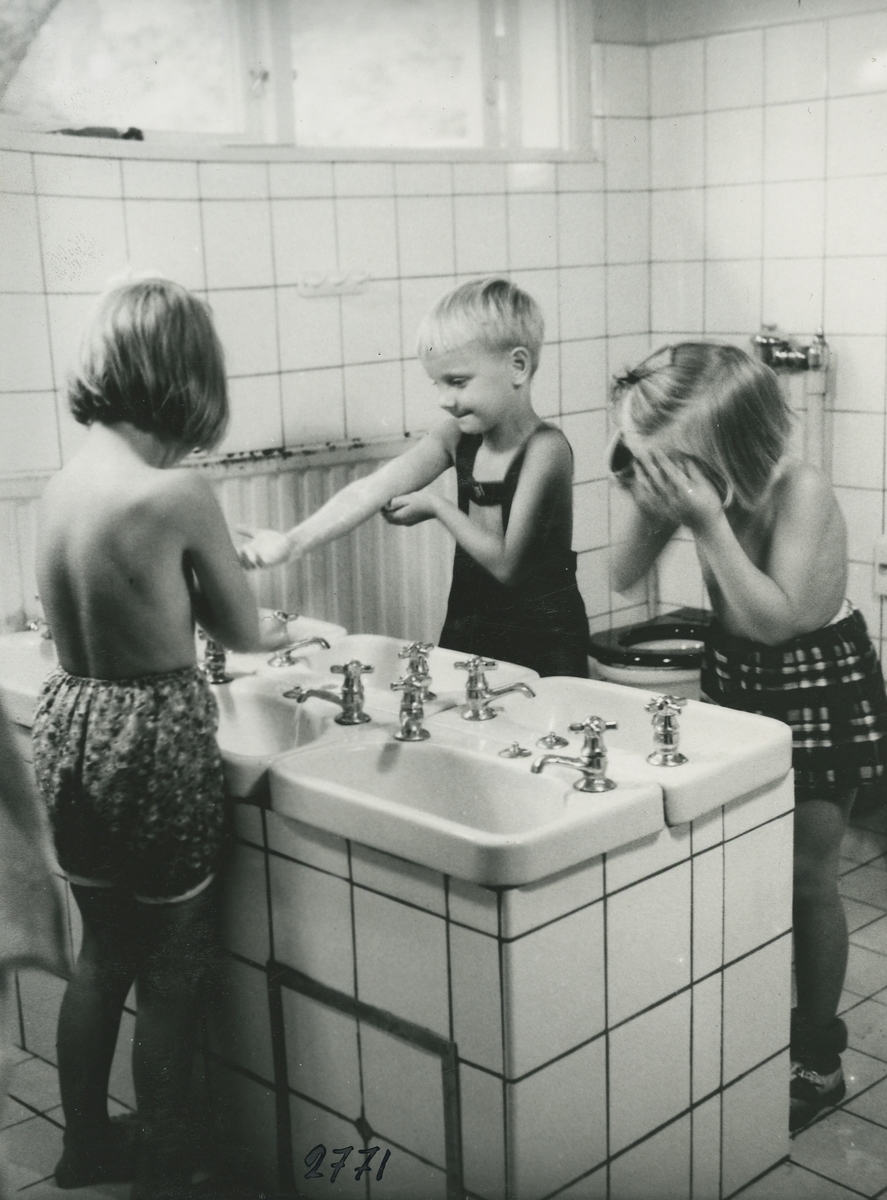 Interiörbild. Daghemmet Blomkulan. Tvagning i tvätt och wc-rum.
Personer: Tre okända barn.