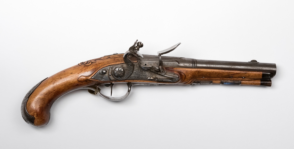 Flintlåspistol signerad "H. Domnerus". Total längd 33 cm, pipans längd 18 cm, slätborrad. Beslag av järn, kaliber 14 mm. Fördsedd med påhängd mässingsbricka märkt "7".
