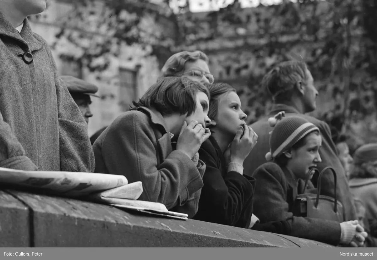 London. Folksamling, unga kvinnor lutar sig mot en mur.