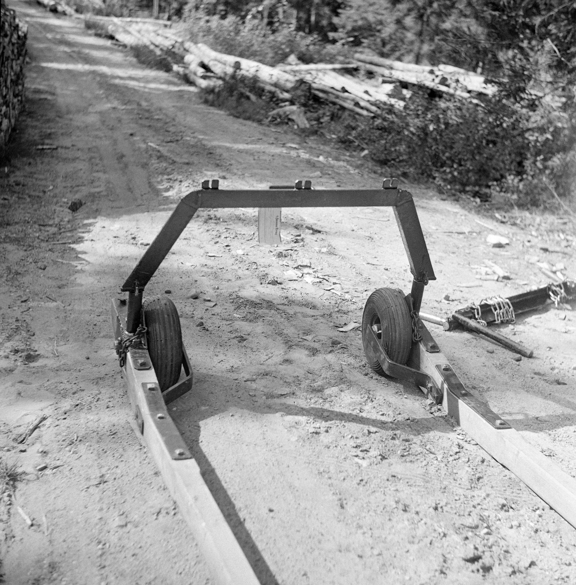 Hjulgående bøyledrag, konstruert av Anton Hansen. Dette er barmarkutgaven av et redskap skogsarbeideren Emil Ruud fra Nord-Odal hadde lansert (1937) for lunning på snødekt mark. Ruuds modell var et redskap der dragarmene (skjækene) var forlenget bakover, slik at de jernbeslåtte bakre endene skulle kunne fungere som meier. Hansen erstattet de jernbeslåtte skåkendene med luftfylte gummihjul. På oversida av dragarmenes ytterender hadde Hansen, som Ruud, festet ei kraftig jernbøyle. Sentralt på toppen av denne bøyla var det påsveiset jernbeslag med hakk for tre snarelenker - kjetttingstumper - som ble viklet et par ganger rundt endene på de stokkene som skulle lunnes. Deretter ble stokkene løftet litt og kjettingene ble festet i hakk i et jernbeslag på toppen av bøyledraget. Dette fotografiet er tatt på en skogbilveg.

Oppfinner: Anton Hansen. Fra «Skogeieren».