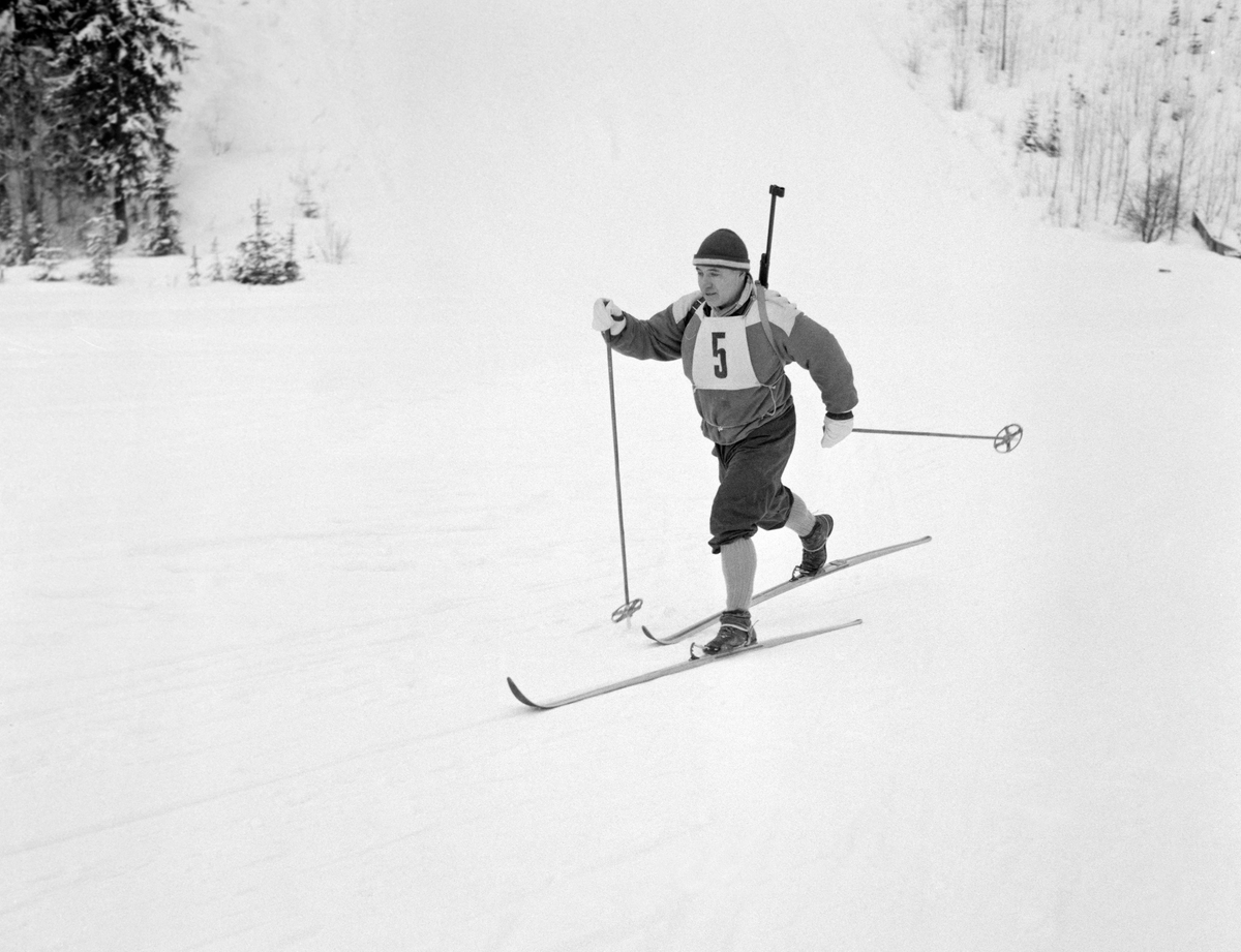 Skiskytteren Jens Kjelsås (1916-2000) fotografert i diagonalgang i flatt lende under kretsmesterskapet i denne øvelsen på Rasta ved Kongsvinger i januar 1961. Løperen gikk på treski med «Rottefella-bindinger» og var kledd i nikkersbukser, overtrekksjakke, topplue og kvite votter.  På brystet hadde han startnummer 5.  Våpenet bar han i en sele på ryggen.  Jens Kjelsås var offiser av yrke, og en dyktig skytter som markerte seg både i militære og i sivile konkurranser.  I skiskyttermiljøet gjorde han seg mer bemerket som leder og organisator enn som utøver, sjøl om oppnådde gode plasseringer i en del lokale konkurranser.  Jens Kjelsås var født i Torsnes i daværende Borge herred utenfor Fredrikstad i Østfold, men arbeidet da dette fotografiet ble tatt som offiser på Terningmoen i Elverum i Hedmark.

Rennet hadde 22 påmeldte og løypa var 8-9 kilometer lang.  Konkurransen, som skal ha vært det første offisielle kretsrennet i skiskyting i denne regionen, gikk i bitende vinterkulde.  Det var 29 minusgrader ved start.  Jens Kjelsås stilte i klassen 42-50 år, og var bestemann der fordi ham var suveren på standplass med 18 treff.  Beste løper uansett alder var Odd Nerby fra Trysil, som hadde bare 16 treff, men en helt annen hastighet i skisporet enn hva Kjelsås hadde.