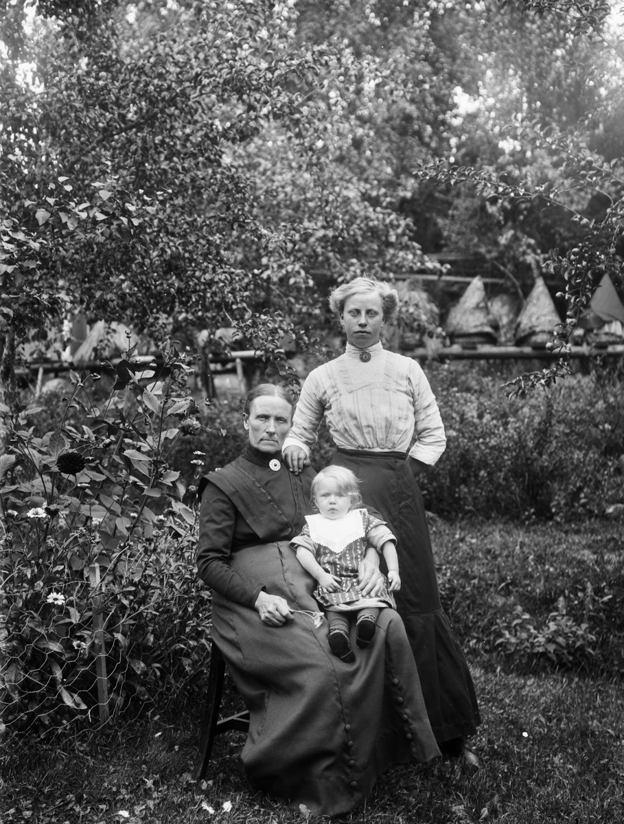 Grupporträtt - äldre kvinna, kvinna och barn i trädgård