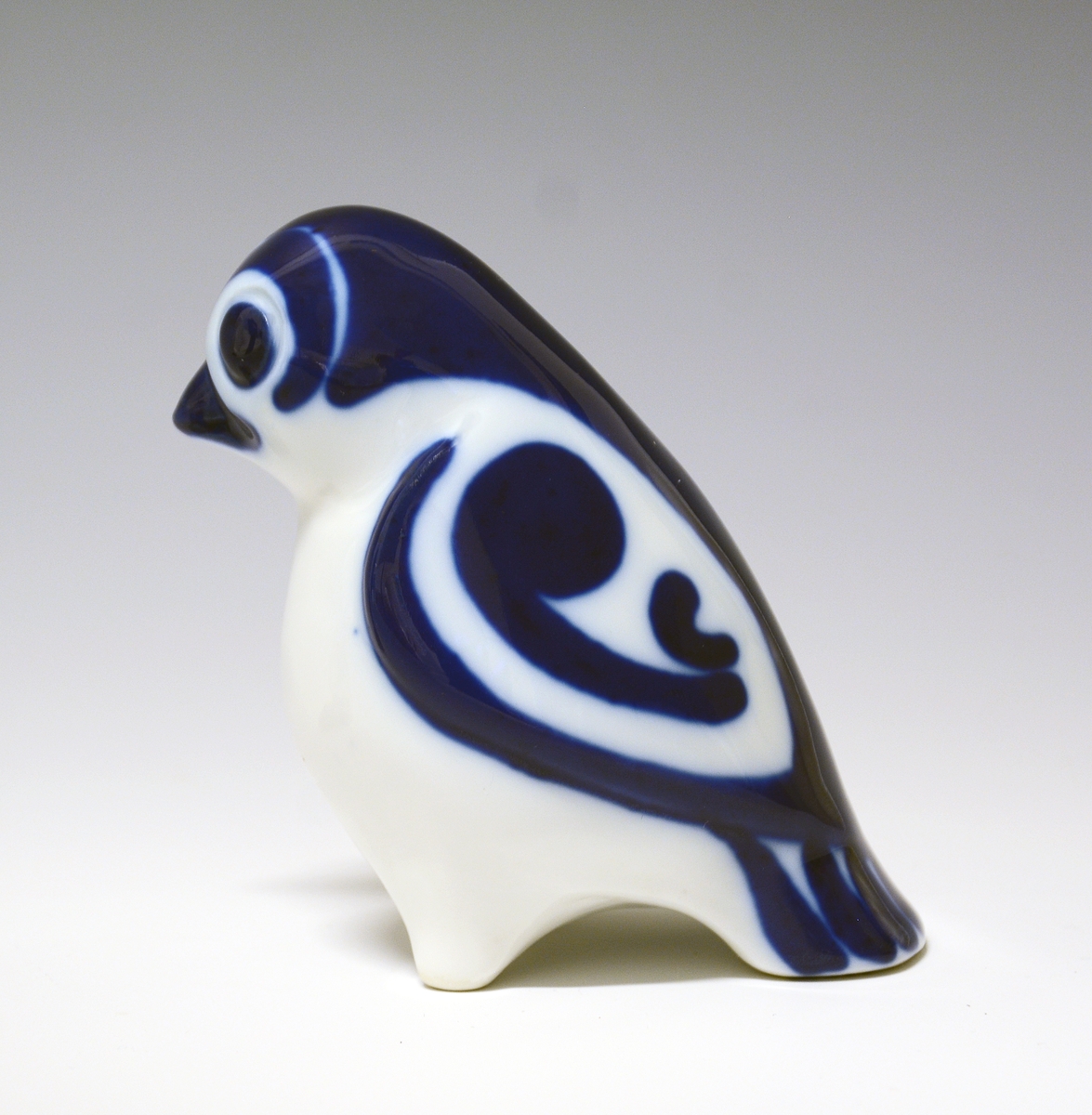Liten fugl av porselen, med hvitt bryst, blå dekor på nebb og fjærdrakt.