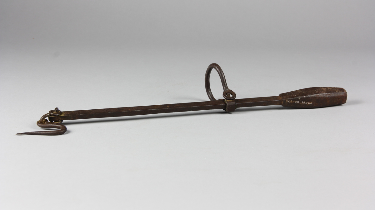 Besman av järn med krok och handtag. Åttkantig klump krönt med år 1836, 26, 9 och justerarmärke TM. Fyrkantig stång med skala fem skålpund.