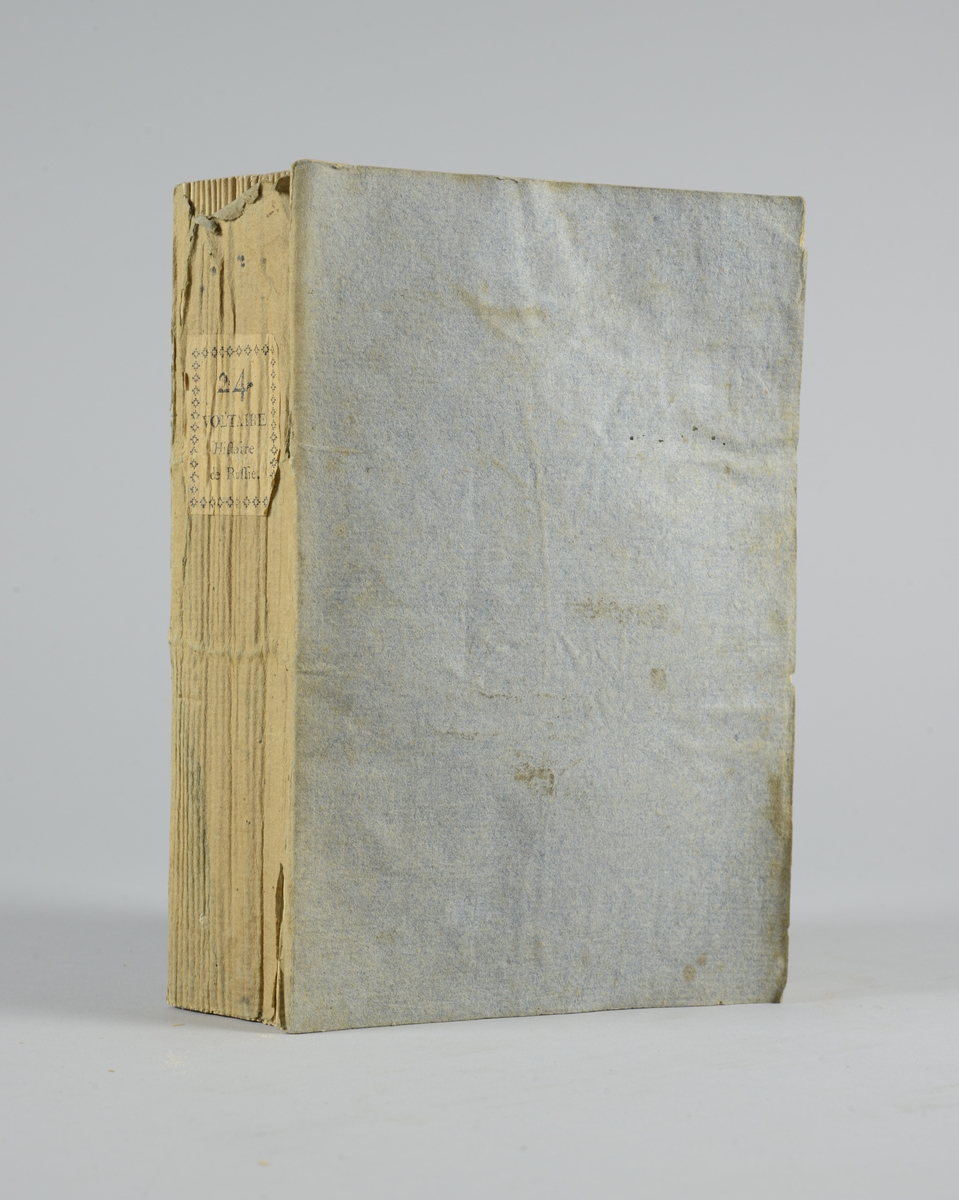 Bok, pappband,"Oeuvres completes de Voltaire", del 24, "Histoire de l´empire de Russie, sous Pierre le Grand ", tryckt 1785.
Pärmen klädd med gråblått papper, skurna snitt. På ryggen klistrad pappersetikett med tryckt text samt volymens nummer. Ryggen blekt.