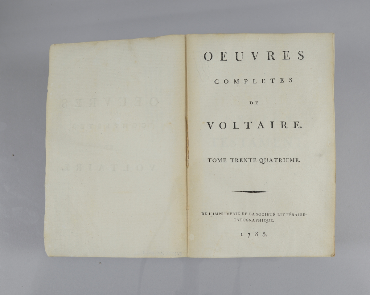 Bok, pappband,"Oeuvres completes de Voltaire", del 34, tryckt 1785.
Pärmen klädd med gråblått papper, på pärmarnas insidor klistrade sidor ur annan bok. Med skurna snitt. På ryggen klistrad pappersetikett med tryckt text samt volymens nummer. Ryggen blekt.