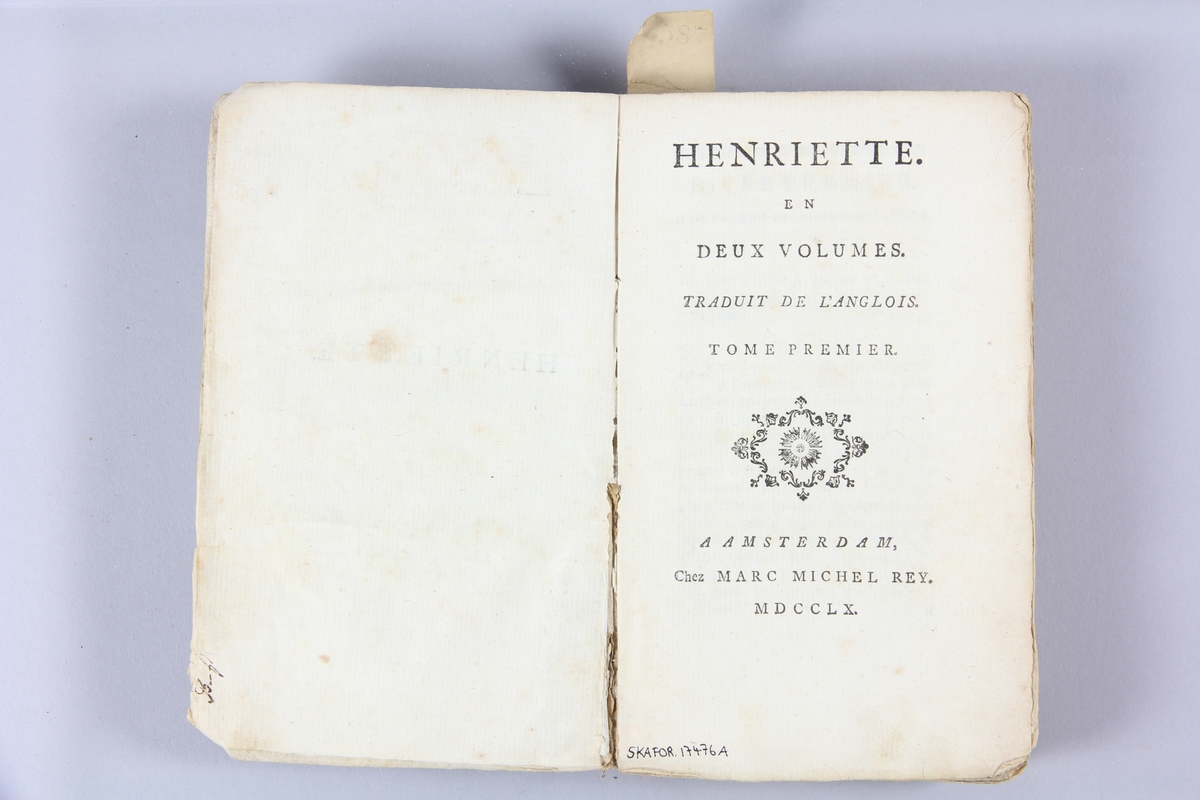 Bok, pappband, "Henriette", del 1, tryckt 1760 i Amsterdam. Pärmar av  gråblått papper, rygg med etikett med bokens titel, delvis svårtolkad. Oskuret snitt. Anteckning om inköp på pärmens insida.