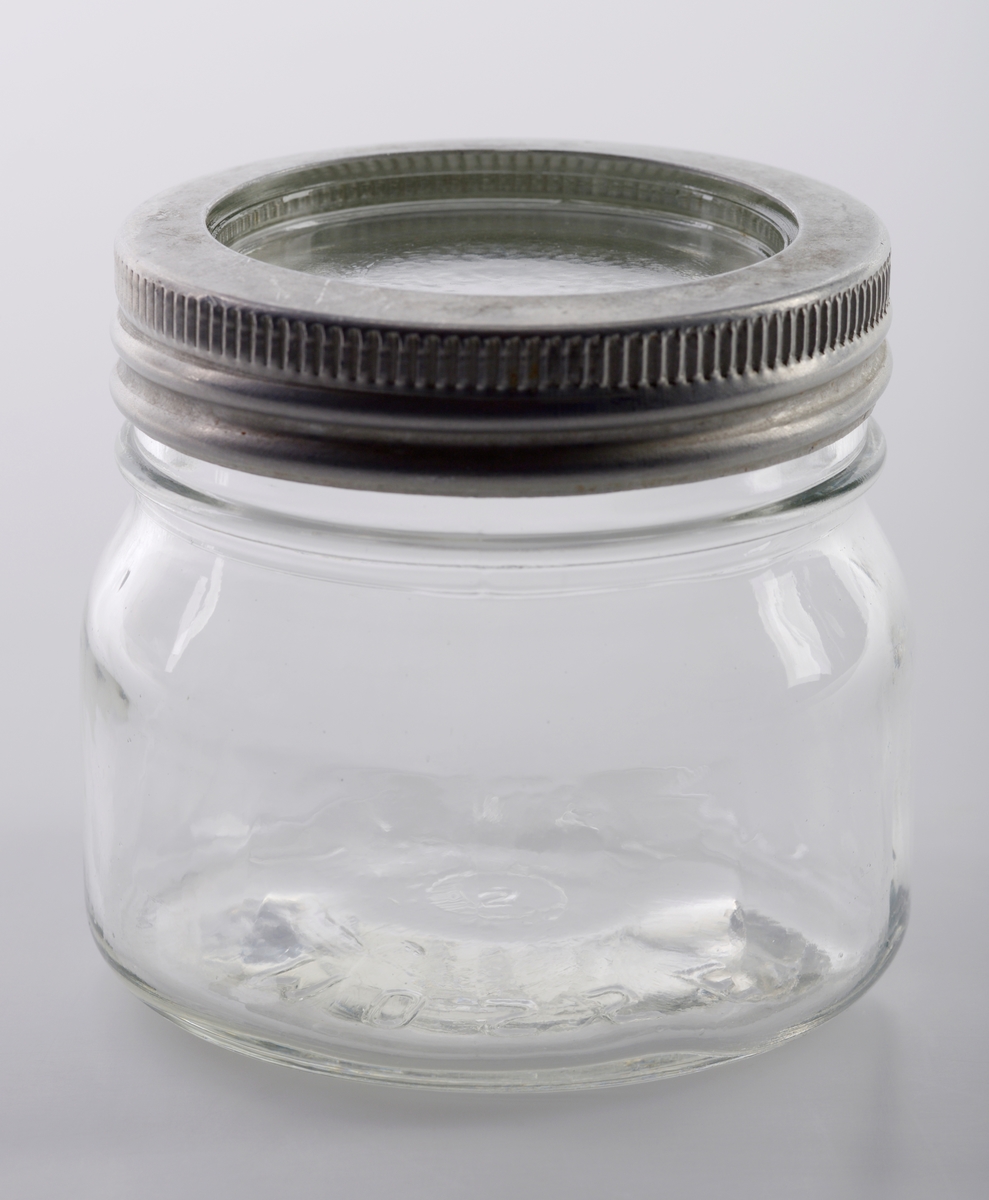 Et "Norgesglass" med løst glasslokk og mansjett laget av aluminium til å skru fast lokket.