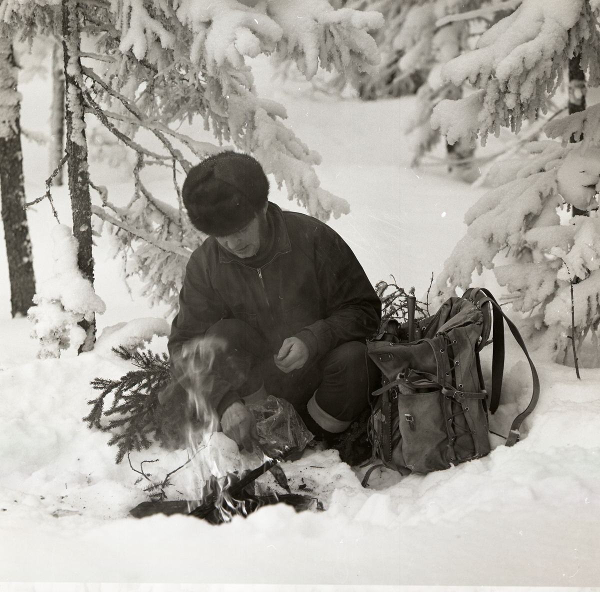 En man sitter på huk i snön och tänder en brasa den 24 februari 1970.