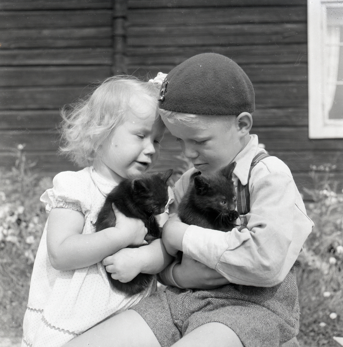 En flicka och en pojke sitter utomhus med varsin kattunge i famnen, 1953.