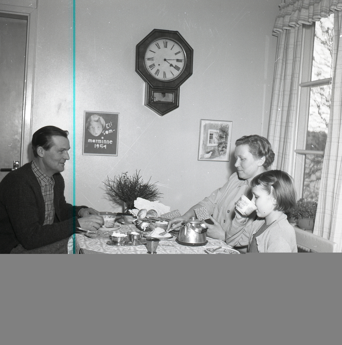 Två vuxna och ett barn sitter vid ett köksbordoch dricker te.