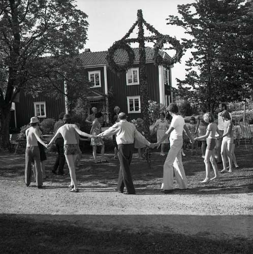 En grupp människor dansar runt midsommarstången vid gården Sunnanåker, 1975.