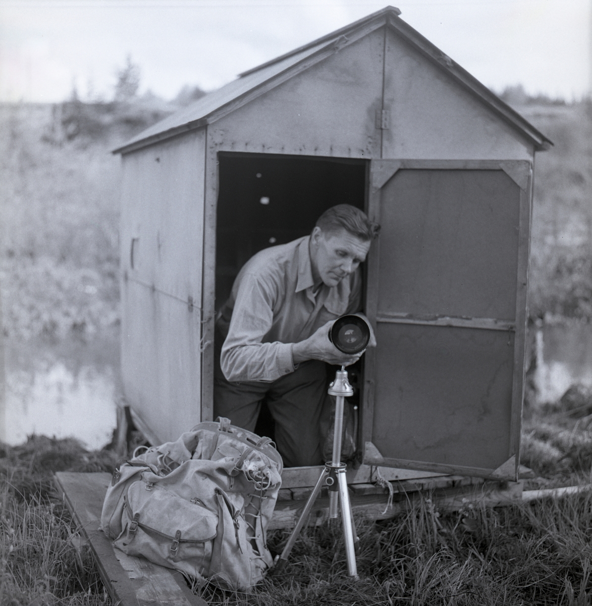 Hilding sitter vid dörren till en orrkoja och placerar sin kamera med teleobjektiv på ett stativ, 1963.