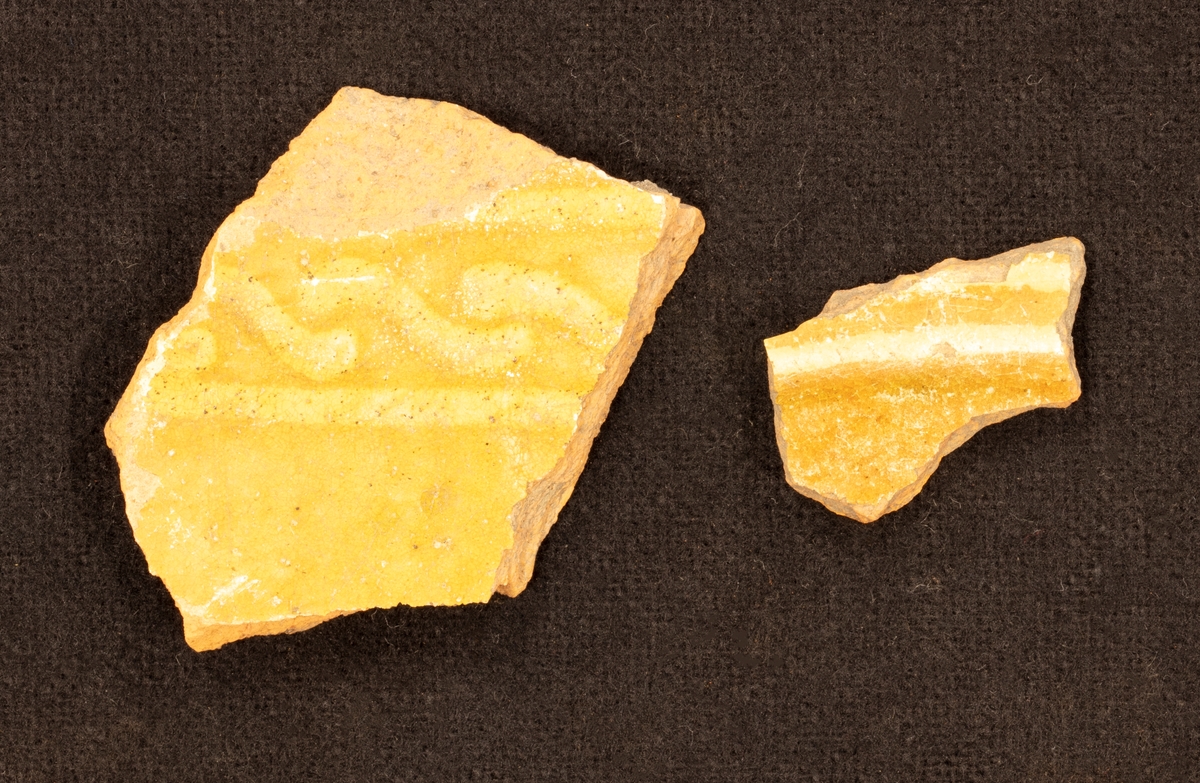 Fragment en skärva av lergods. Gulgrön glasyr. Två parallela, gula sträck med vågor som krokar i varandra i mellan sträcken.

Funnen i anläggning S9.
Grävningsledaren ändrade sedan anläggningsbeteckningen i grävrapporten till K9.
Fynden kommer från en arkeologisk utgrävning/schaktövervakning av Brätte 1:8 ledd av Oscar Ortman 2018.