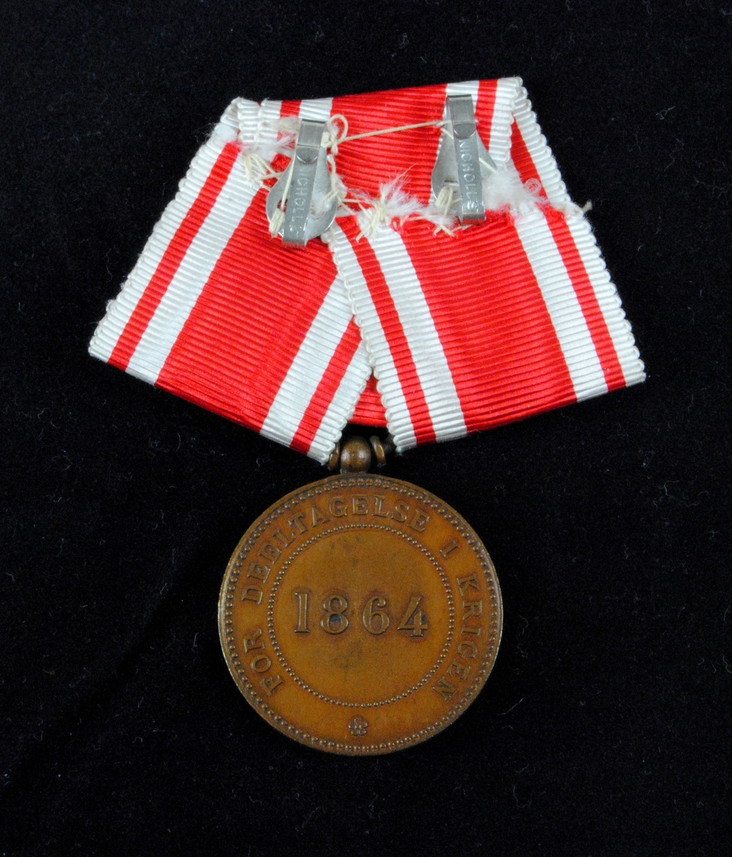 "Erindringsmedalje for Krigen 1864". Medaljen pryds av Christian IX:s profil i relief. Medaljen har ett röd- och vitrandigt ordensband.