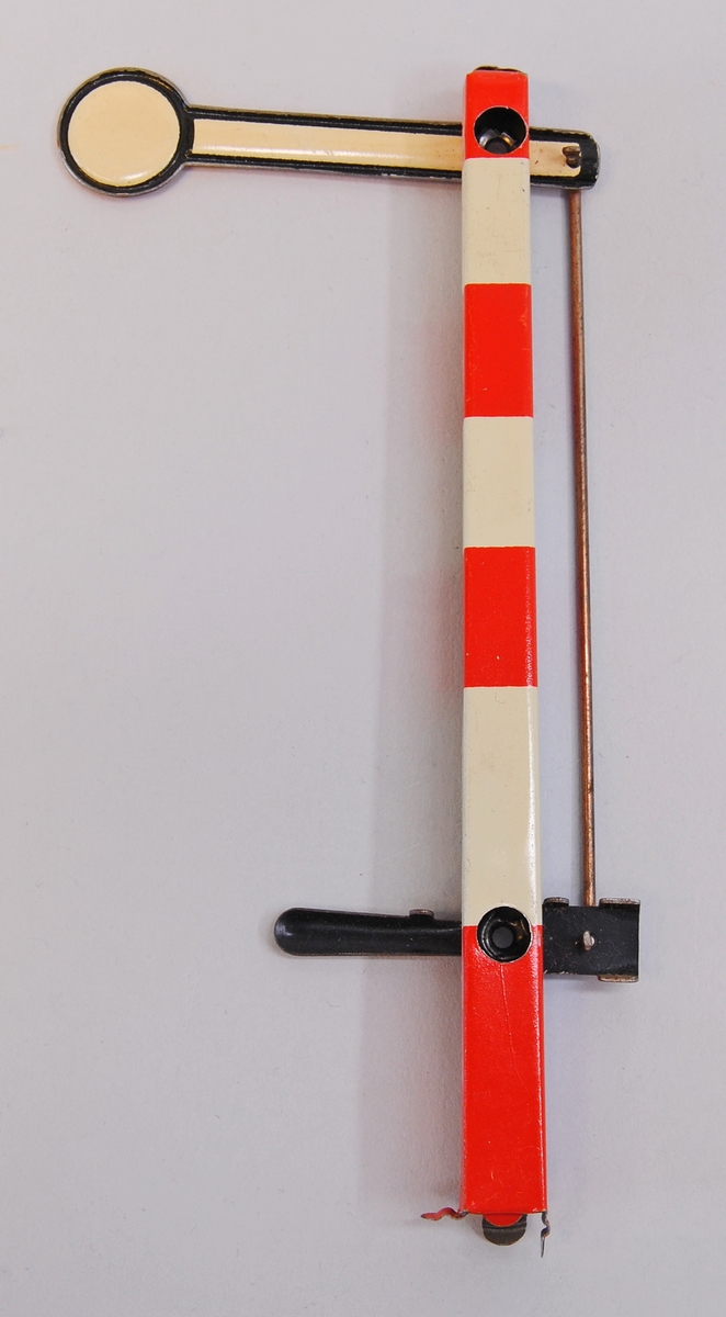 Semafor till modelljärnväg i 0-skala (skala 1:43-1:48) i bleckplåt. Semaforstolpen är målad i rött och vitt (svagt gultonat) och har en manöverspak i svart. Själva semaforarmen är vit med röda kanter på ena sidan och vit med svarta kanter på den andra.