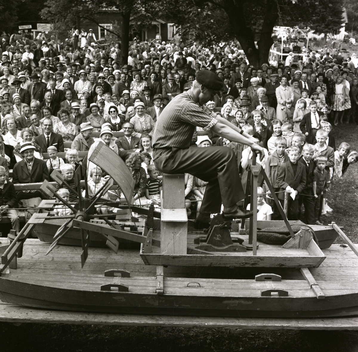 En man uppträder sittandes på en trampbåt i samband med Hembygdsfestens karneval i Rengsjö, 22 juli 1962.