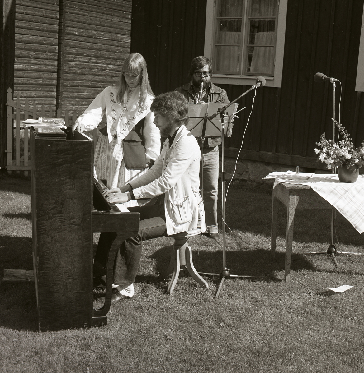 Tre personer musicerar under Rengsjöfesten 16 juli 1978. En man spelar på ett piano medan en kvinna iförd folkdräkt står bredvid och bakom henne står ytterligare en man som spelar flöjt.