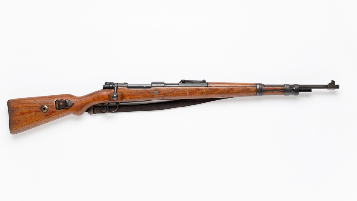 Gevær i tre og metall med lærrem. Diverse stempler. Våpenet har både tysk og norsk merking. 

Karabiner 98 kurz (K98k) er en tysk rifle med boltmekanisme, designet av Mauser og innført i Wehrmacht i 1935.
De Mausere som ble ombygd til 7,62 x 63 mm blir gjerne kalt HV-Mauser eller Heimeverns-Mauser. Disse kjennes på at de er stemplet med kaliber 7,62 og enten HÆR, FLY eller K.ART fulgt av et nytt serienummer gitt etter ombygging.