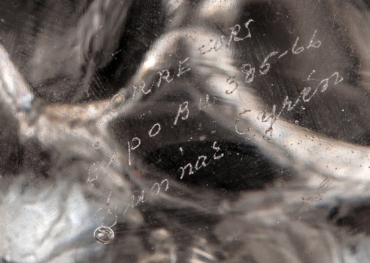 Stor flaska i klarglas med blåsta bulor i tre rader runt om hela flaskans kropp.
Graverad märkning under botten:
ORREFORS
Expo bu 385-66
Gunnar Cyrén