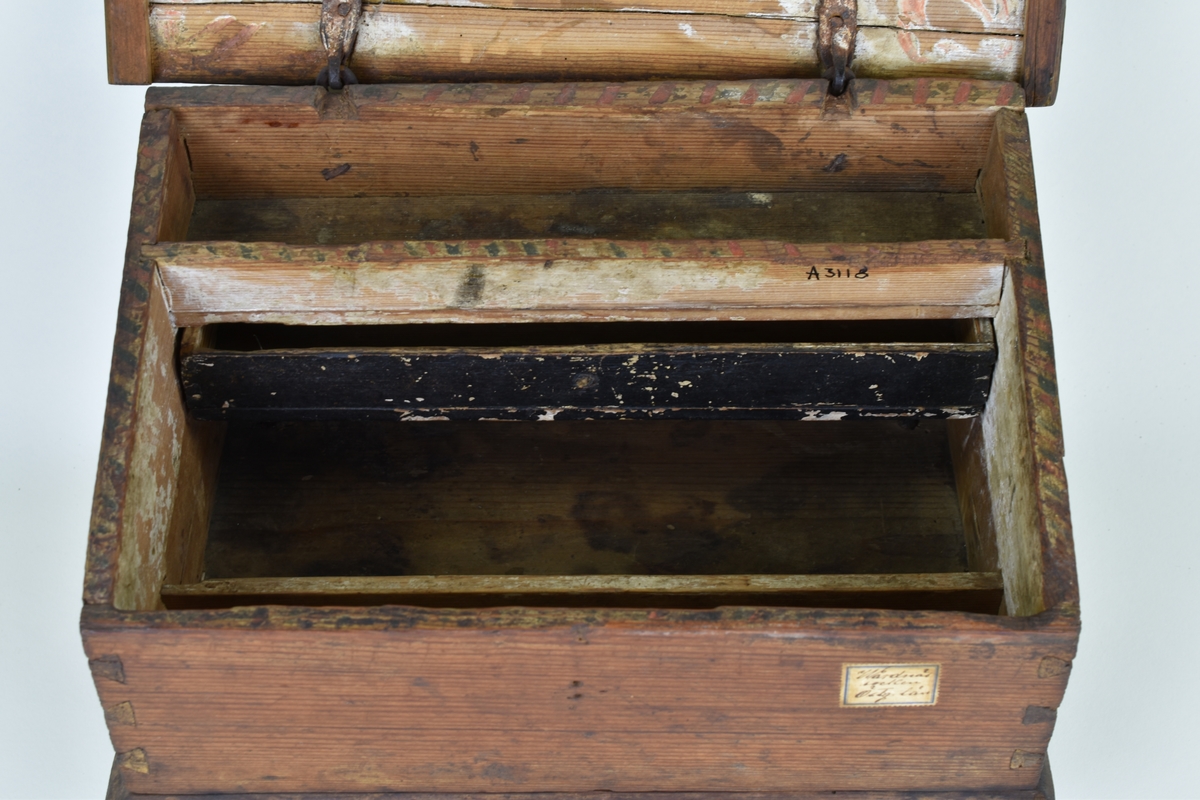 Skrin av furu med pulpetlock och inredning med fack och låda. På utsidan brunmålat och blomstermotiv på locket. På lockets insida bemålat med årtalet 1766 inom en krans.