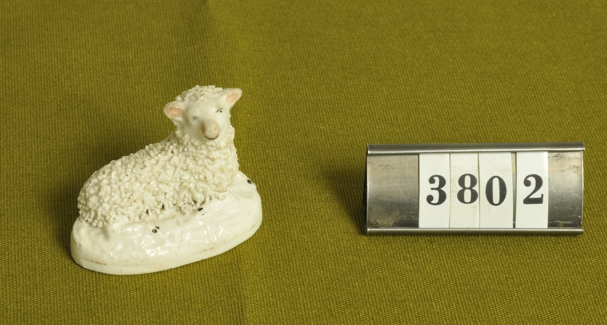 Figur i form av liggande lamm.
