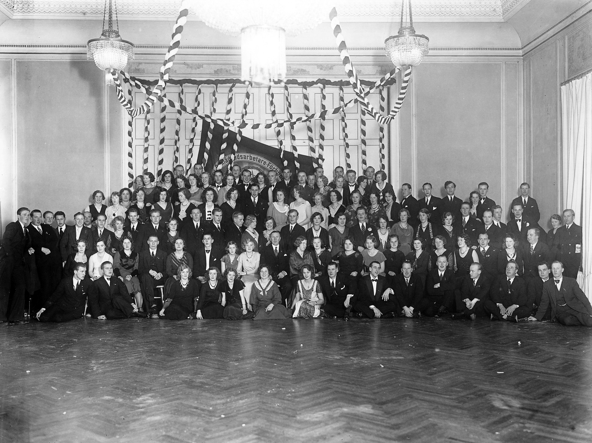 Ett hundratal kvinnor och män ur Svenska Beklädnadsarbetarförbundets Alingsåsavdelning poserar vid avdelningens 10-års jubileum 1932.
Svenska Beklädnadsarbetarförbundets Alingsåsavdelning.
10-års jubileet 1932.