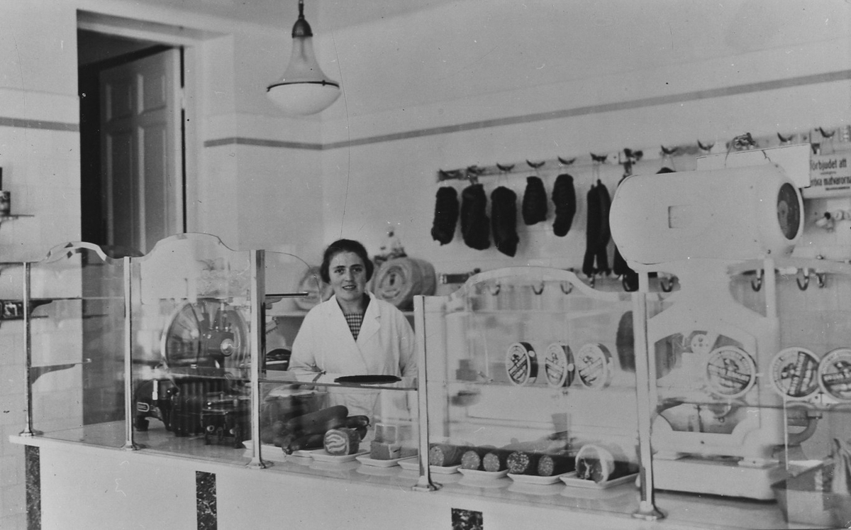 En kvinna står bakom en charkuteridisk i Skoglunds Charkuteri.
Nygatan 13. Kvarteret Storken.
Interör från butiken.