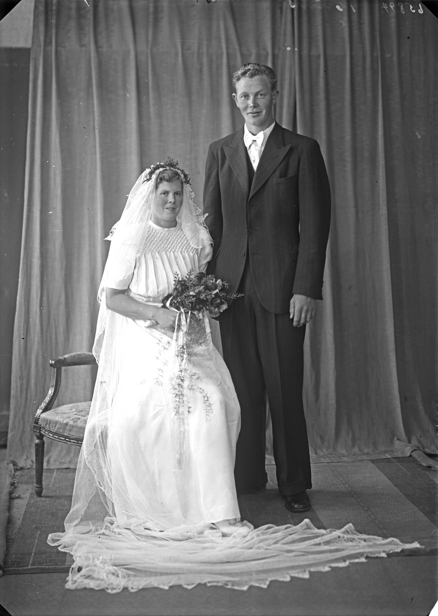 Portrett. Ung kvinne i hvit brudekjole med blomsterbukett og ung mann i mørk dress. Brudepar. Bestilt av Nils Nesse. Våga. Sveio