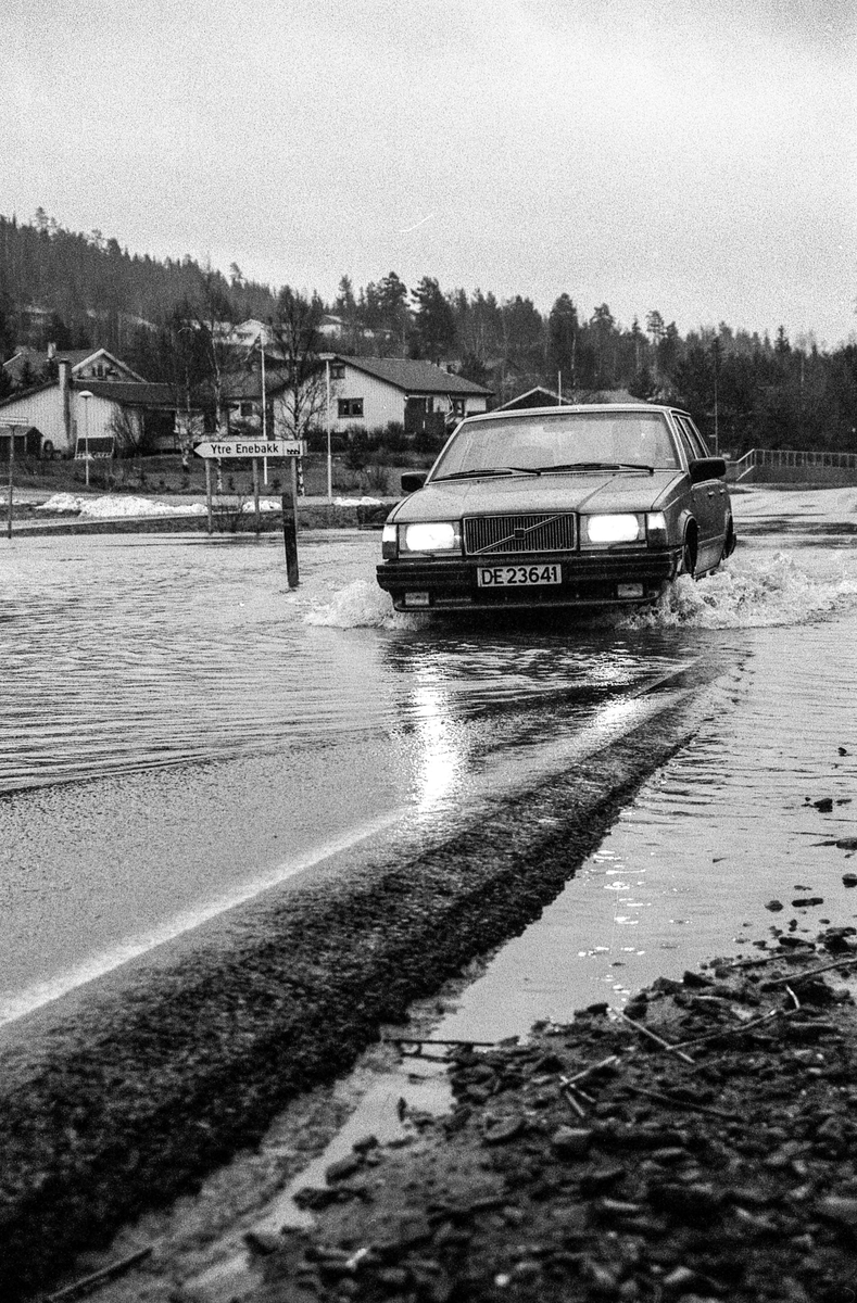 Flomskader på veiene, Riksvei 120, Ytre Enebakk. Vannet flommer over veier og jorder, biler kjører så vannspruten står.