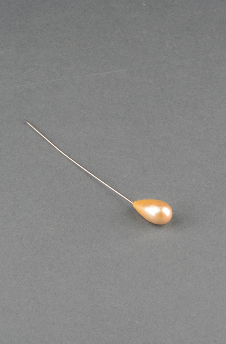 Hattenål i stål med dråpeformet perle i ene ende. Perle utført i ukjent material og bemalt.