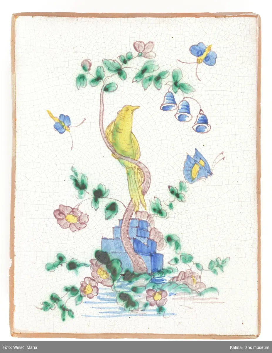 KLM 24452. Kakel. Rektangulär kakelplatta till flat ugn. Vit krackelerad glasyr med dekor i grönt, blått, gult och rosa. Dekoren består av ett handmålat motiv föreställande en gulgrön fågel på ett blommande träd samt blå fjärilar.