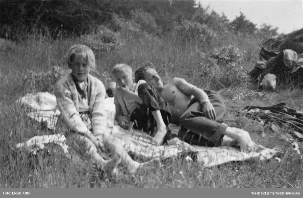Far og barn på teppe i fjelllandskap.