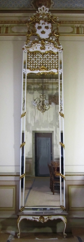 Spegel i rokokostil. Spegeln består av grundspegel och krön (:1) samt ett konsolbord (:2). Krönet har vapnet "Tre kronor" med omgivande dekorationer i form av blad, blommor och annat. De är utförda i gips på trägrund. Övriga delar, från botten upp till vapnets fäste, är utförda i trä och pastellage med blad skurna i trä. Spegeln är troligtvis tillverkad på 1800-talet.