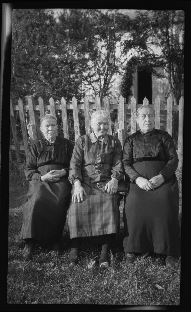 Gruppeportrett av tre eldre damer sittende utendørs.