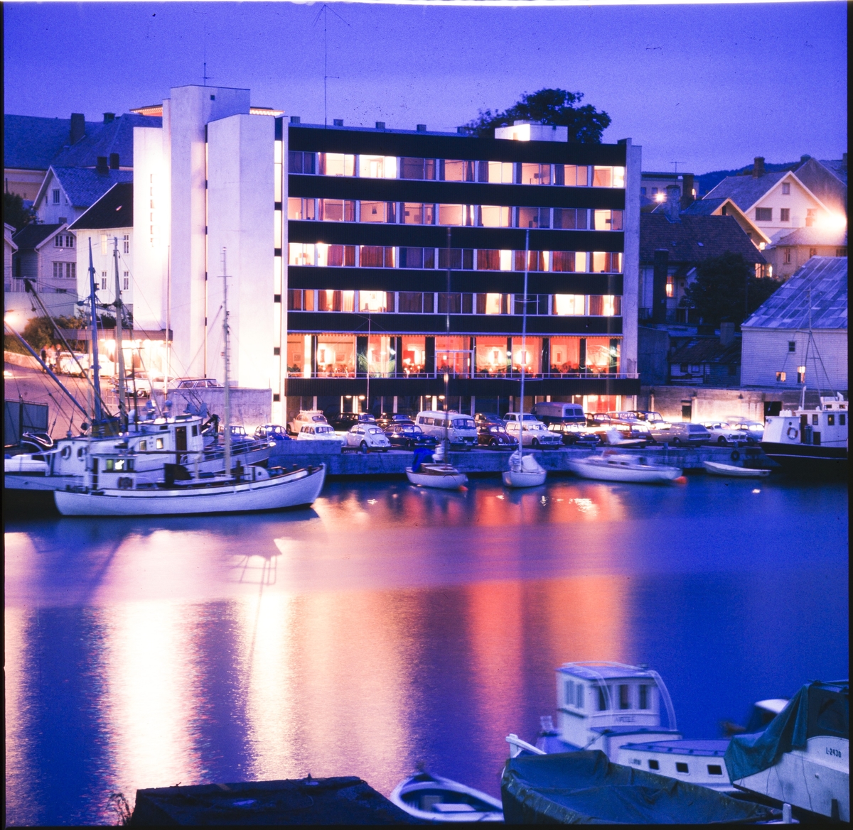 Hotel La Mer i Haugesund tatt over Smedasundet fra Risøy. Senere kjent som Hotell Maritim. Bildet er tatt i kveldslys. En fiskebåt ligger i forgrunnen.