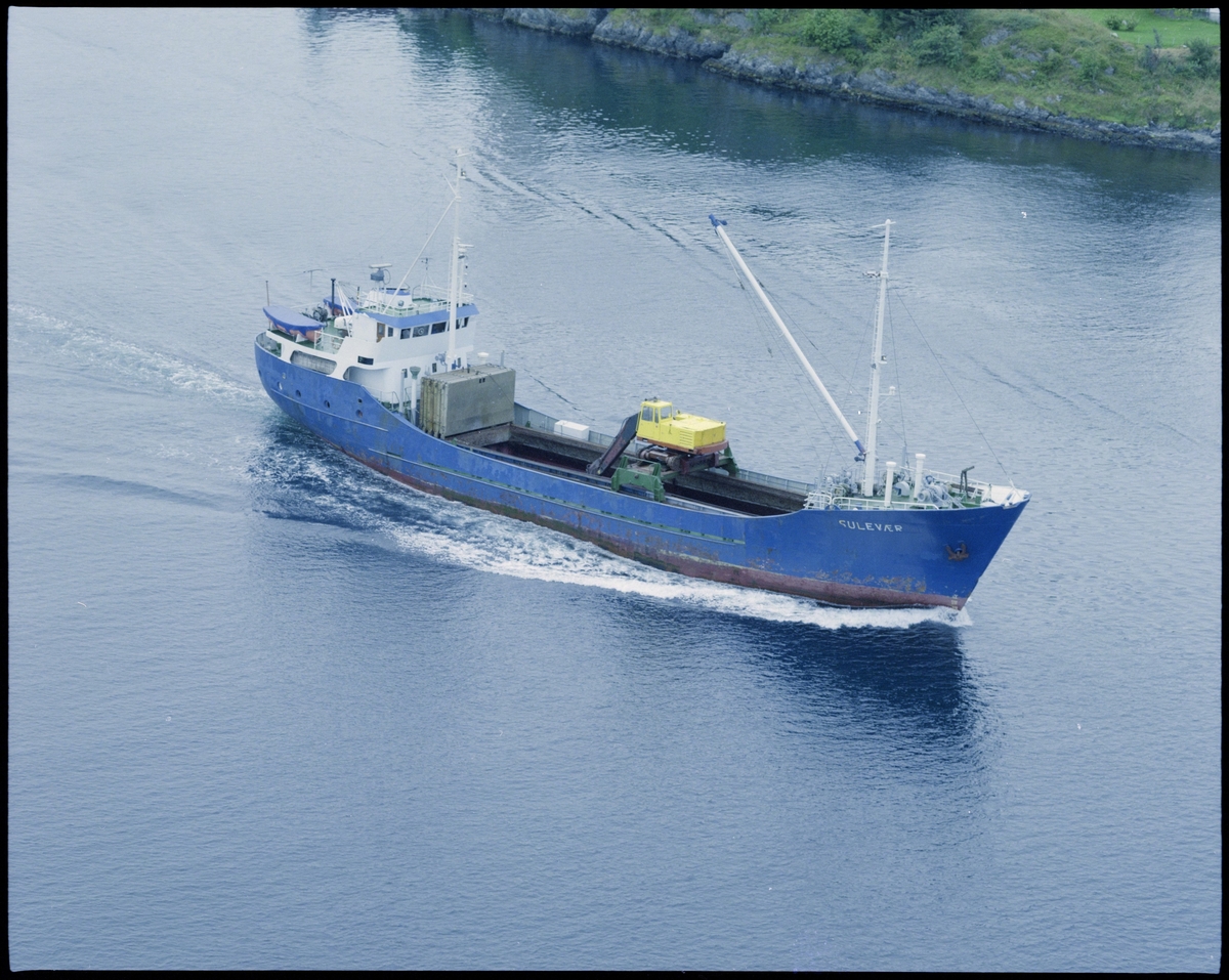 Bulkskipet M/S "Sulevær" i fart langs land. Det er festet en gravemaskin til en ramme over skipets lasterom.