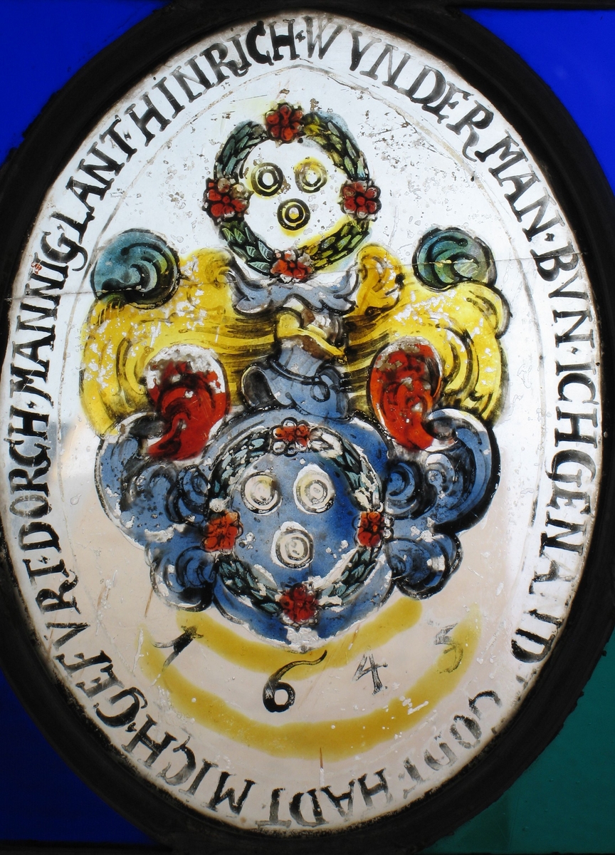 2  blomsterkranser, hver med to ringer, mellom disse  bølgende former i blått, rødt og oker, årstallet  1645.  Tekst rundt bildemotivet.