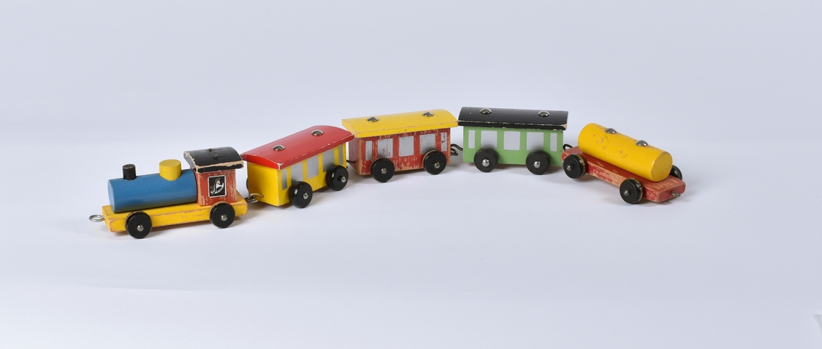 Leketog; lokomotiv og fire vogner. Treleker med hjul. Disse hektes sammen med metallring og krok. De ulike togvognene er malt i forskjellige klare farger.