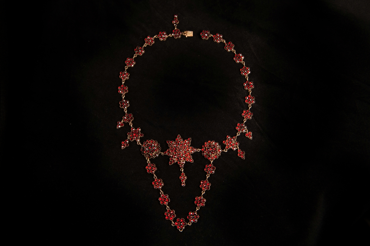 Granathalsband med slipade röda granater, infattade i koppar. 
Halsbandet består av "blommor" i länk, med två större "blommor" i mitten, omgivande en stjärna med hänge. Från de två större blommorna hänger ner en blomlänk.

Halsbandet förvaras i rektangulär bleckplåtsask, fylld med vadd.