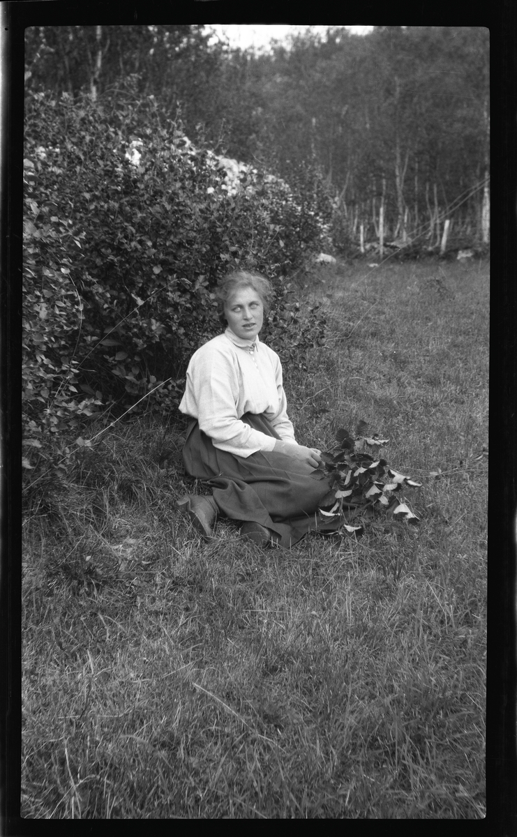 Portrett av  ung kvinne sittende på gressmark.