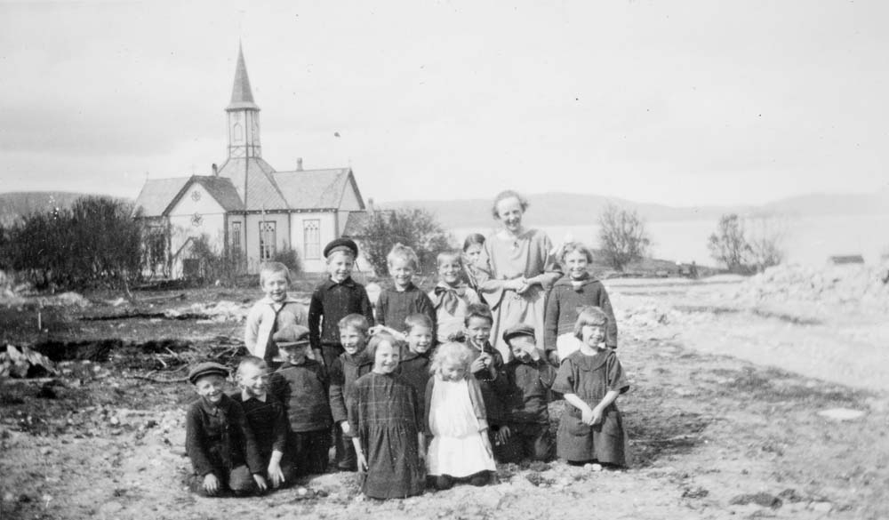 Gruppebilde med en kvinne og mange glade barn. Sandnessjøen / Stamnes kirke i bakgrunnen.
