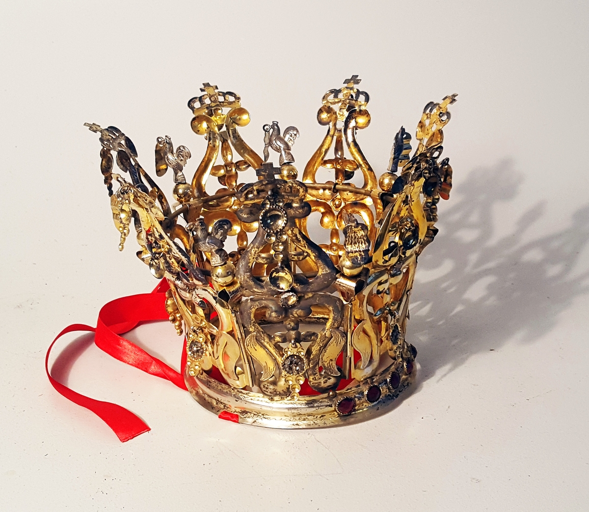 
1 brudekrone av sølv.

Brudekrone av sølv. Kronen bærer guldsmed Bør' stempel, nemlig T.B. - 13 1/2 - 62. (1862)
Hele kronen forgyldt undtagen 7 haner. I kronen indsat hvite og røde stener samt paasat løv, hvori filigranarbeide. Til et rødt silkebaand, der er knyttet rundt kronens nederste kant er paasyd 9 kulørte, mønstrete silkebaand, der hænger ned over brudens ryg. Kronen er vel vedlikeholdt og typisk god.
Kjøpt av lærer Thomas Buttedal, Holmedal, Søndfjord.  