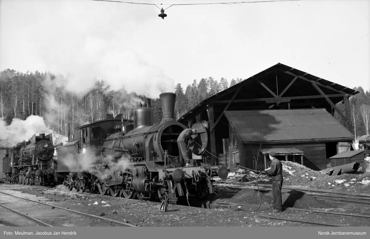 Damplokomotiv type 18c nr. 212, feiing av kjelrør ved lokomotivstallen på Hønefoss stasjon. I bakgrunnen et damplokomotiv type 30.