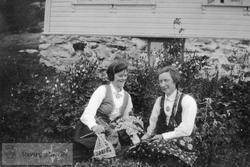 To bunadskledde kvinner foran hus