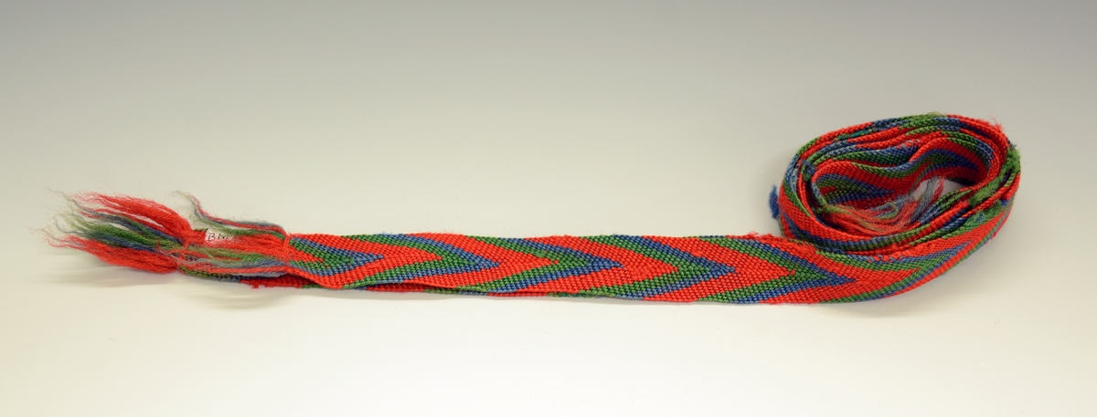2 stk sokkebånd.Slengde. Mønsteret danner stripet spiss mot midten. Renning: 12 grønne, 11 blå, 21 rødetråder. Fra protokoll.